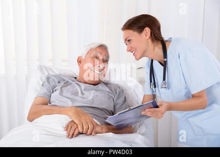 Junge weibliche Krankenschwester mit Zwischenablage Besuchen ältere männliche Patienten Stockfoto