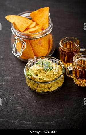 Bier und eine Schüssel mit Guacamole mit Nachos auf einem alten schwarzen Holztisch in einem Pub Stockfoto