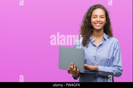 Junge Hispanic woman holding Computer Laptop mit einem glücklichen Gesicht stehen und lächelnd mit einem selbstbewussten lächeln zähne Stockfoto