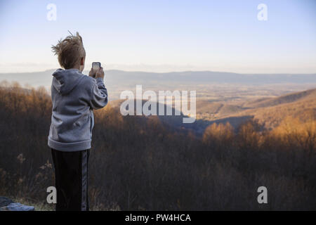 Ansicht der Rückseite des jungen Fotografieren mit dem Mobiltelefon beim Stehen auf Berg gegen den klaren Himmel Stockfoto