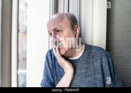 Alte älterer Mann, während das Fenster Verwirrung und allein zu Hause in alternden Ruhestand Witwer Demenz und Alzheimer Konzept deprimiert. Stockfoto