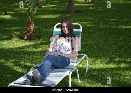 Junge Frau in einem wunderschönen Garten von grünem Gras Ausruhen vor einem Pool Stockfoto
