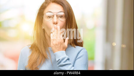 Frau mittleren Alters tragen wolle Pullover und coole Brille deckt Mund in Schock, blickt schüchtern, Stille und Fehler Konzepte, Angst Stockfoto