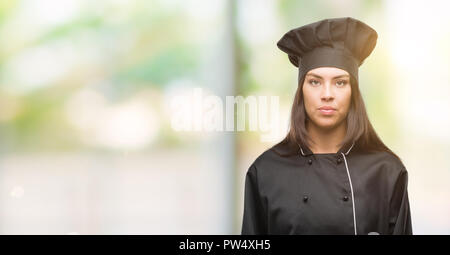 Junge hispanic Koch Frau Koch Uniform mit einem selbstbewussten Ausdruck auf Smart Face denken Ernst Stockfoto