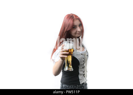 Eine junge, hübsche Frau mit langen roten Haaren in einem traditionellen deutschen Korsett Getränke eine goldene Bier aus einem Glas Stockfoto