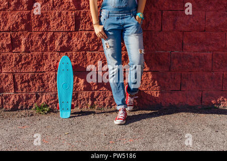 Close up Füße eines Mädchens in rote Turnschuhe und Blue Penny Skate Board mit rosa Räder neben der Wand stehen. Städtische Szene, Leben in der Stadt. Sport, Fitness Stockfoto