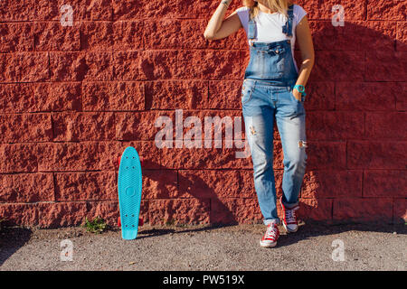 Close up Füße eines Mädchens in rote Turnschuhe und Blue Penny Skate Board mit rosa Räder neben der Wand stehen. Städtische Szene, Leben in der Stadt. Sport, Fitness Stockfoto
