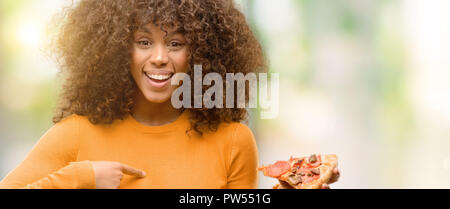 Afrikanische amerikanische Frau mit einer Pizza mit Überraschung Gesicht zeigenden Finger zu sich selbst Stockfoto