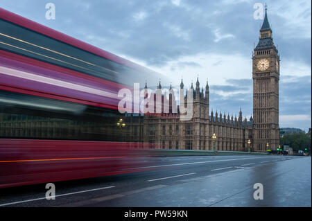 Ein Doppeldecker-bus kreuzt die Westminster Bridge in London bei Sonnenaufgang. Keine Menschen, niemand. Beleuchtete Big Ben Tower mit der Uhr auf der linken Seite. Nasse ebnen Stockfoto