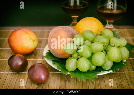 Still life: Auf dem Tisch auf einer Platte sind Früchte, neben zwei Gläser Wein. Stockfoto
