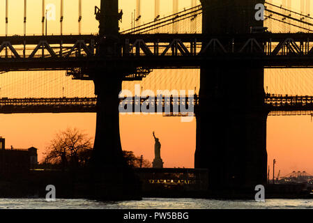 11-2017 New York, USA. Die Brooklyn und Manhattan Bridge bei Sonnenuntergang, mit der Freiheitsstatue. Vögel und Möwen fliegen Overhead, die aussehen wie du Stockfoto