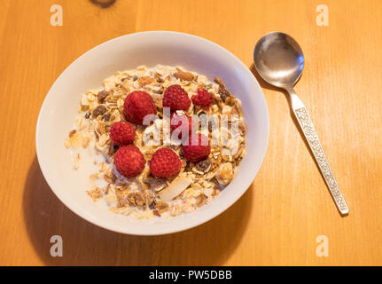 Gesundes Frühstück, eine Schale mit frischen Himbeeren und Müsli mit Milch, gegen eine Holz Hintergrund gesehen. Stockfoto