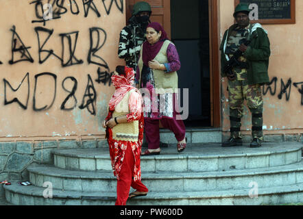 Srinagar, Kashmir. 13. Oktober, 2018. Der Wähler geht aus einem poling Station bei J&K städtischen lokalen Körper Umfragen Abstimmungen in der dritten Phase, wie indische trooper Guard steht, während in 13 Jahren. Kaschmir unter fester Sicherheit und einer separatistischen gesponserten herunterfahren. Behörden bereitgestellt werden Zehntausende zusätzliche Soldaten in den bereits hoch militarisierten Region für die Wahlen, die in vier Phasen festgehalten werden. Am Montag Morgen in muslimisch dominierten Gebieten Tal. eine Ausgangssperre war in der Tat im alten Teil der Stadt von Srinagar anti-Indien Proteste zu verhindern. © sofi Suhail/Alamy leben Nachrichten Stockfoto