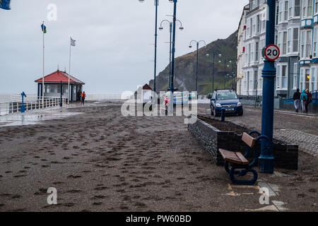Aberystwyth, Wales, UK. 13. Oktober, 2018. UK Wetter: Nach einer Nacht, der starken Winde und Gezeiten im Zusammenhang mit dem Sturm Callum, der Promenade in Aberystwyth ist in Hunderte von Tonnen von Sand und Kies bedeckt. Mit einer weiteren Flut an diesem Morgen, und die Winde wieder über 50 mph wehenden, weitere Schäden zu rechnen ist. Foto: Keith Morris/Alamy leben Nachrichten Stockfoto