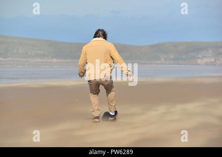 Brean Sands Beach, Brean, Burnham on Sea, Somerset, England, Großbritannien, 13.. Oktober 2018, Wetter: Mann jagt seinen Hut, nachdem er von starken Winden des Sturms Callum weggeblasen wurde. Stockfoto