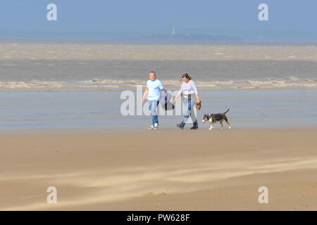 Paar, die mit einem Hund am Strand von Brean Sands, Brean, Burnham on Sea, Somerset, England, Großbritannien, warmer sonniger und windiger Oktobertag. Stockfoto