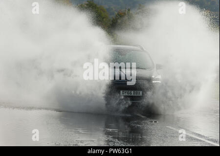 Llangattock, Powys, Wales, UK. 13. Oktober, 2018. Die Autofahrer fahren Sie durch Hochwasser an der A40 in der Nähe von brede und Llangattock in Powys, Wales, UK. Sturm Callum weiter South Wales zu vernichten, als den Fluss Usk platzt es Banken als Folge der massiven sintflutartige Regenfälle in Powys Überschwemmungen viele Riverside Eigenschaften. © Graham M. Lawrence/Alamy Leben Nachrichten. Stockfoto