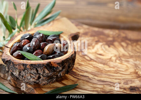 Frische braune kalamata Oliven und Blätter in Olivenholz Schüssel Stockfoto