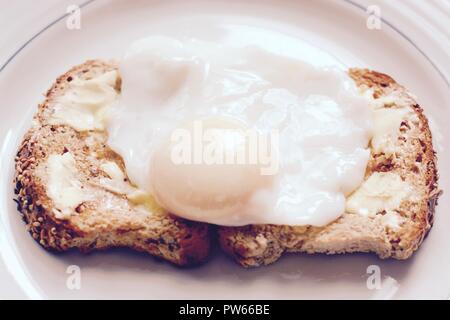 Die perfekt pochierte Eier auf Gesäte gebuttertem Toast braun-Filter angewendet Stockfoto