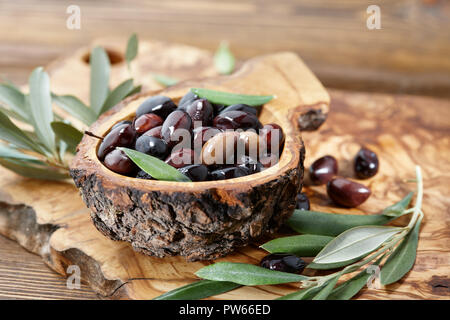 Frische braune kalamata Oliven und Blätter in Olivenholz Schüssel Stockfoto