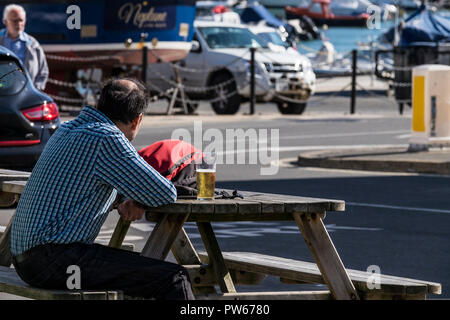 Ein Mann, der an einem Tisch sitzen mit einem Pint Lager außerhalb eine Kneipe in der Küstenstadt Lyme Regis in Dorset. Stockfoto