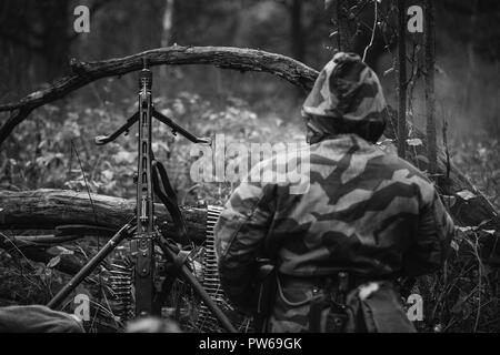 Versteckte unbekannte Re-Enactor als Deutsche Wehrmacht Soldat mit Maschinengewehr in einen Hinterhalt in Wald gekleidet. Foto in den Farben Schwarz und Weiß. Stockfoto