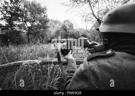 Versteckte unbekannte Re-Enactor als Deutsche Wehrmacht Infanterie Soldat im Zweiten Weltkrieg Soldat sitzend mit Maschinenpistole in einen Hinterhalt in Wald angezogen Stockfoto