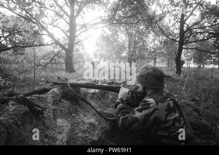 Nicht identifizierte Re-Enactor verkleidet als Soldat der deutschen Wehrmacht Infanterie im zweiten Weltkrieg versteckt sitzen mit Gewehr Waffe In einem Hinterhalt In Graben im Herbst Stockfoto