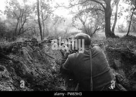 Nicht identifizierte Re-Enactor verkleidet als Soldat der deutschen Wehrmacht Infanterie im zweiten Weltkrieg versteckt sitzen mit Gewehr Waffe In einem Hinterhalt In Graben im Herbst Stockfoto