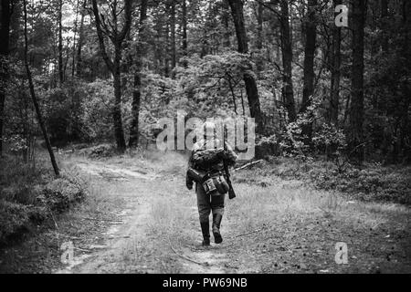 Re-Enactor gekleidet, wie Deutsche Wehrmacht Infanterie Soldat im Zweiten Weltkrieg marschiert zu Fuß entlang der Forststraße im Sommer Tag. Foto in Schwarz und Weiß Co Stockfoto