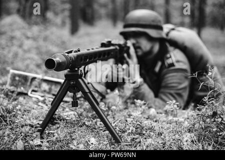 Versteckte unbekannte Re-Enactor gekleidet, wie Deutsche Wehrmacht Soldat ein Maschinengewehr auf gegnerische aus Graben im Wald. Foto in Schwarz und Weiß Stockfoto