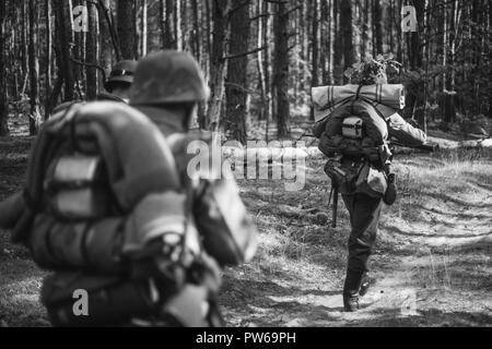 Re-enactors gekleidet, wie Deutsche Infanterie Soldaten im Zweiten Weltkrieg marschiert zu Fuß entlang der Forststraße im Sommer Tag. Foto in den Farben Schwarz und Weiß. Stockfoto