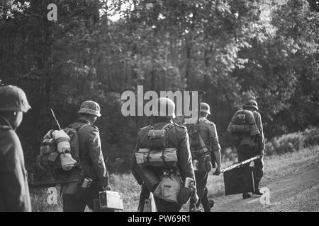 Re-enactors gekleidet, wie Deutsche Infanterie Soldaten im Zweiten Weltkrieg marschiert zu Fuß entlang der Forststraße im Sommer Tag. Foto in den Farben Schwarz und Weiß. Stockfoto