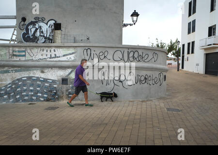 Ein Mann in Shorts und violettem Hemd geht an feministischen Graffiti auf Carrer de Bellavista, Es Castell, Menorca, Spanien vorbei Stockfoto