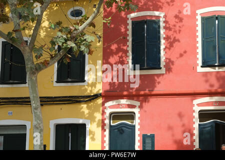 Schatten von Bäumen fallen über die bunten Reihenhäuser und Fensterläden in der Carrer Victori, Es Castell, Menorca, Spanien Stockfoto