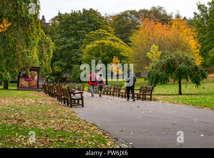 Menschen zu Fuß vorbei an Holzbänken im Princes Street Gardens mit Herbst Blatt Farben, Edinburgh, Schottland, Großbritannien Stockfoto