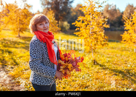Frau mittleren Alters holding Bouquet von Herbst Zweige mit gelben und roten Blätter. Stilvolle Dame Wandern im Wald Stockfoto