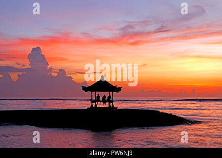 Drei Personen in einem Balinesischen Pagode auf Sanur Strand bei Sonnenaufgang, Strand von Sanur, Bali, Indonesien sitzen Stockfoto