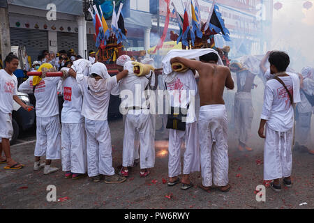 Palanquin-Träger bei einer Prozession während des Vegetarian Festival in Phuket Town, Thailand, die sich vor explodierenden Feuerwerkskörpern schützen Stockfoto