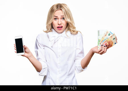 Frustrierte Frau zuckte mit den Schultern, Anzeigen Handy leerer Bildschirm und Halten von Lasten von Euro-banknoten vor weißem Hintergrund. Große Telefonrechnung Stockfoto