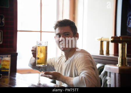Glückliche junge Mann trinkt Bier in der Kneipe. Der Mann an der Pint Bier, Stockfoto