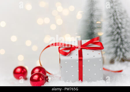 Elegante Silber Geschenkbox mit roter Seide Schleife winter Szene im Wald mit Tannen gebunden Spielereien im Schnee. Weihnachten Neue Jahre präsentiert holiday Magi Stockfoto