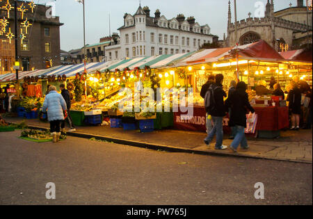 Die Käufer auf dem Weihnachtsmarkt in die Hauptstadt der Grafschaft Cambridgeshire Universität Cambridge England Großbritannien mit beleuchteten Marktstände Stockfoto