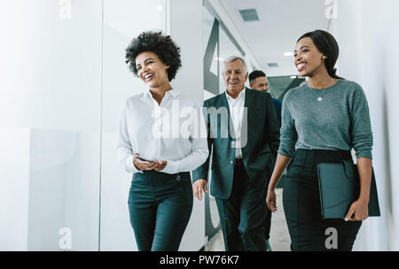 Vielfältige Gruppe von Geschäftsleuten zu Fuß durch Büro Flur. Das Team von Corporate Fachleute gehen und Sprechen in modernen Büro Flur. Stockfoto