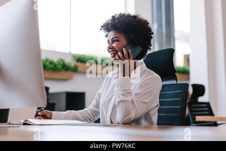 Lächelnde Frau, die an ihrem Schreibtisch sitzt und telefoniert. Geschäftsfrau, die einen Anruf von ihrem Schreibtisch im Büro aus macht. Stockfoto