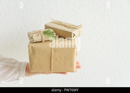 Junge Frau hält auf gestreckte Hand Geschenkboxen in Handwerk Papier mit Garn gebunden. Weißer Hintergrund Pastellfarben. Weihnachten Neue Jahre präsentiert Co Stockfoto