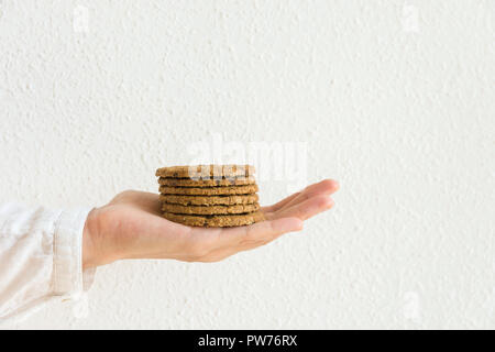 Junge kaukasier Frau hält in gestreckter Hand des Chocolate Chip Cookies mit Hafer- Muttern an der weißen Wand Hintergrund stack. Urlaub Backen gesund Pas Stockfoto