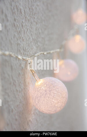 Weihnachten Neujahr Hintergrund. Hängende Pastell Golden Baumwolle Kugeln Girlande weiße Wand im Hintergrund. Im skandinavischen Stil. Glitzernde Lichter. Gemütliche Festliche ein Stockfoto