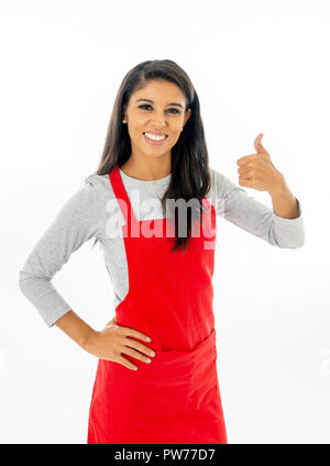 Portrait Of Happy stolz schönen lateinischen Frau trägt eine rote Schürze kochen lernen mit dem Daumen, die Geste in Kochkurse für kleine Unternehmen und hom Stockfoto