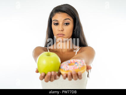 Schöne junge Frau versucht, die Wahl zwischen Apple und Krapfen in Gesund ungesunde Nahrung, Detox essen, Kalorien und Diät Konzept zu machen. Stockfoto